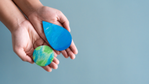 A pair of hands together palms up with cut out pieces of paper that had been coloured on. One with an Earth, the other with a water drop. Symbolising to save water, to save the environment.